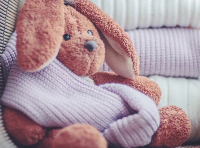 brown floppy ear bunny plush toy wearing light purple knit sweater closeup