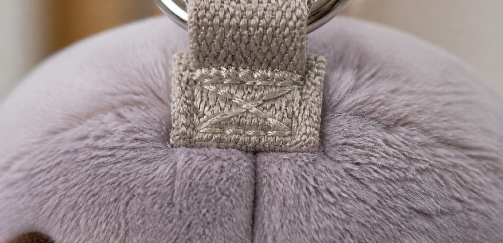 Macro view of a reinforced plush keychain anchor point showing the webbing loop base and locked reinforcement stitching where the hardware attaches
